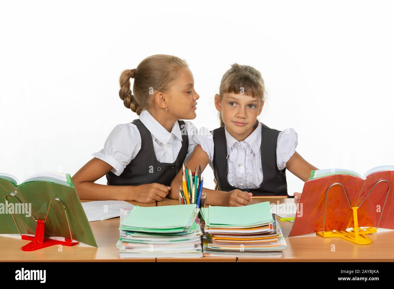 Les filles sont assis à un bureau de l'école, l'un à l'autre chuchote quelque chose dans l'oreille Banque D'Images
