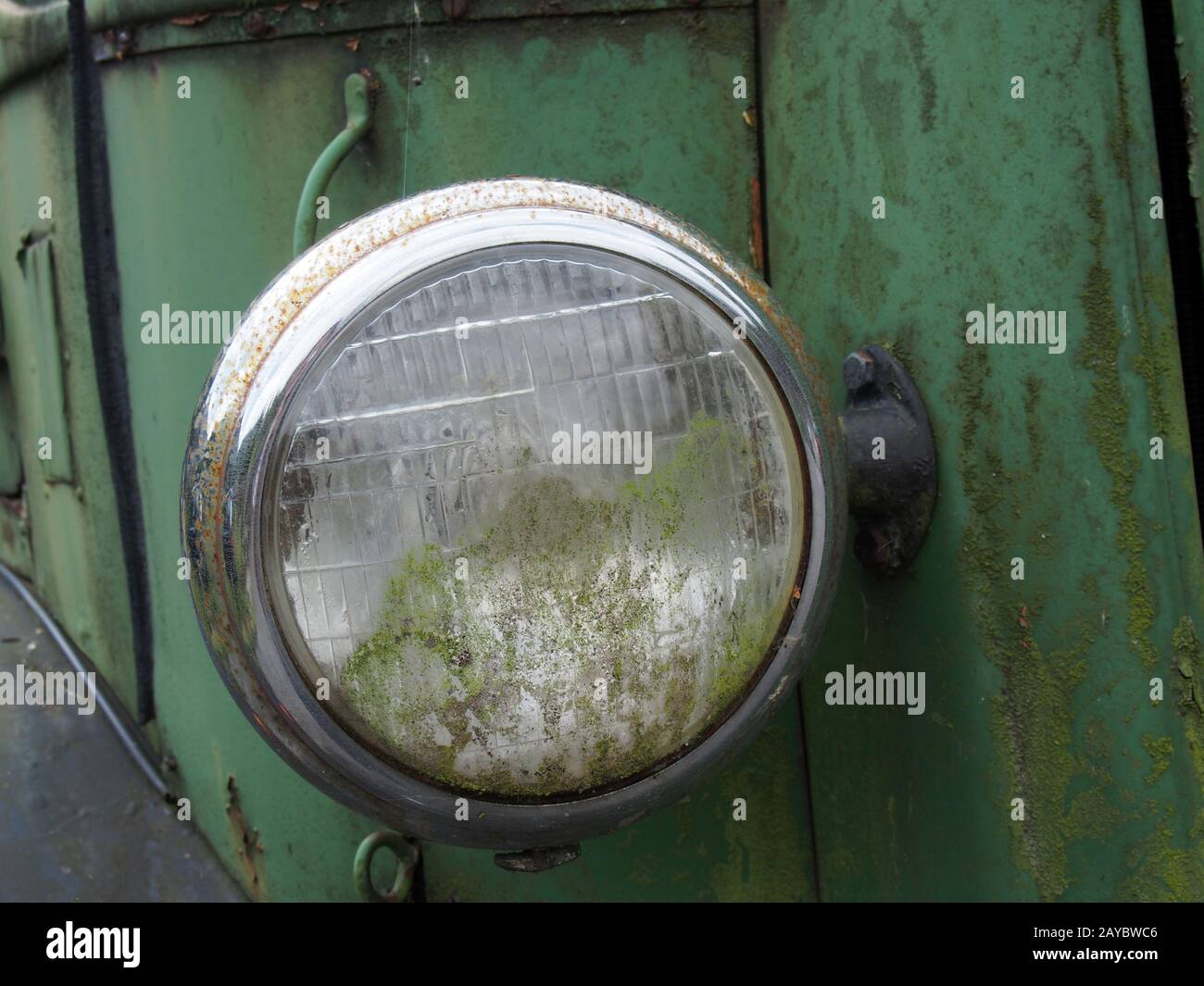 gros plan sur le phare d'un vieux camion abandonné avec grille et panneaux verts rouillés Banque D'Images