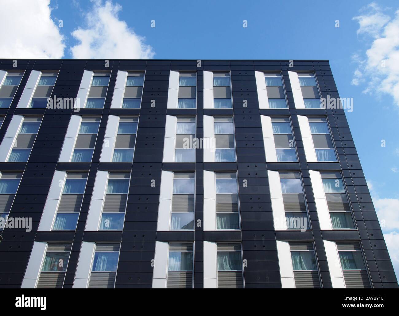 vue vers le haut de l'angle d'un immeuble de bureaux moderne noir avec ciel bleu et nuages reflétés dans de grandes fenêtres en verre Banque D'Images