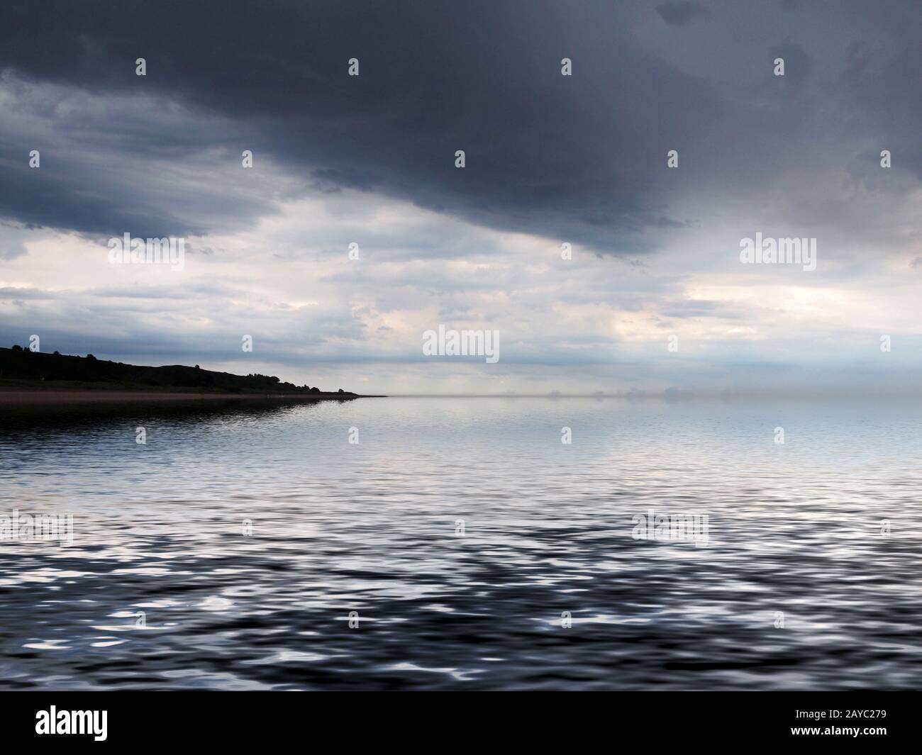 une côte lointaine reflétée dans la mer avec des nuages sombres spectaculaires Banque D'Images