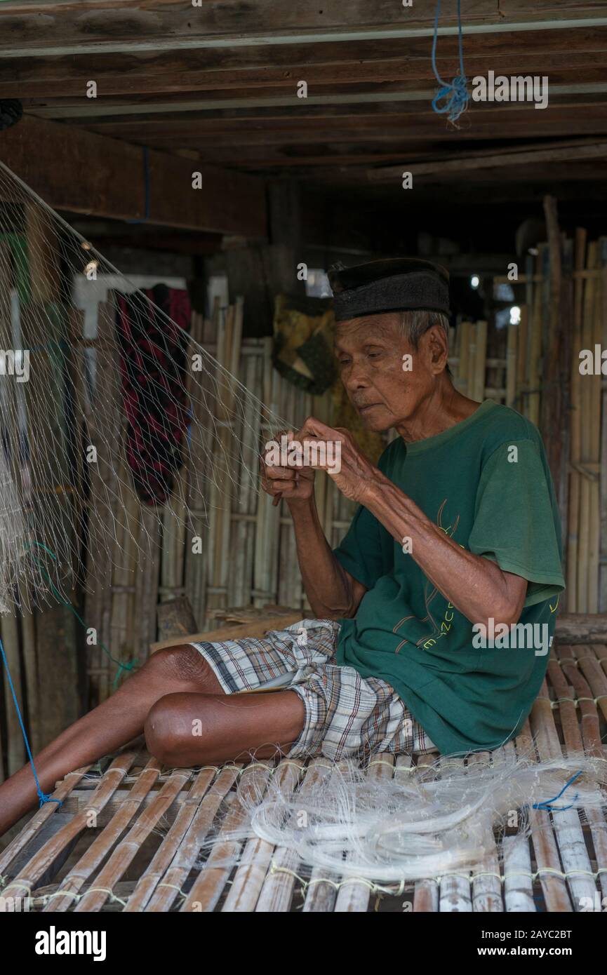 Une scène de village avec un homme local faisant un filet de pêche dans le village bojau Sea Gypsy sur l'île de Bungin, célèbre pour vivre dans des maisons stilt au-dessus de l'eau Banque D'Images