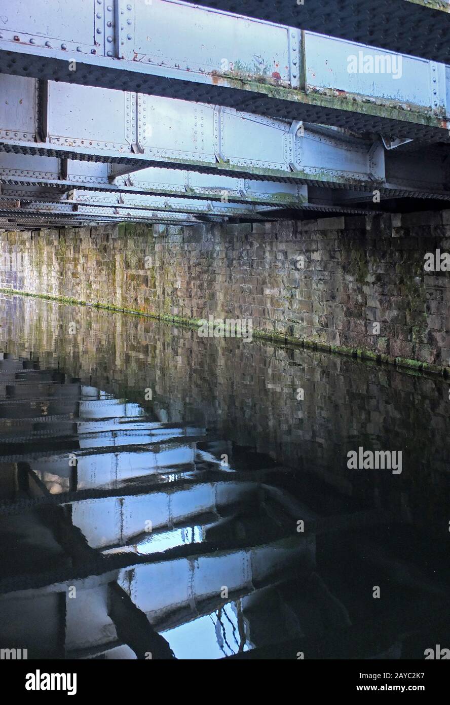 les vieilles poutres en acier se reflètent dans l'eau d'un canal sombre sous un pont Banque D'Images