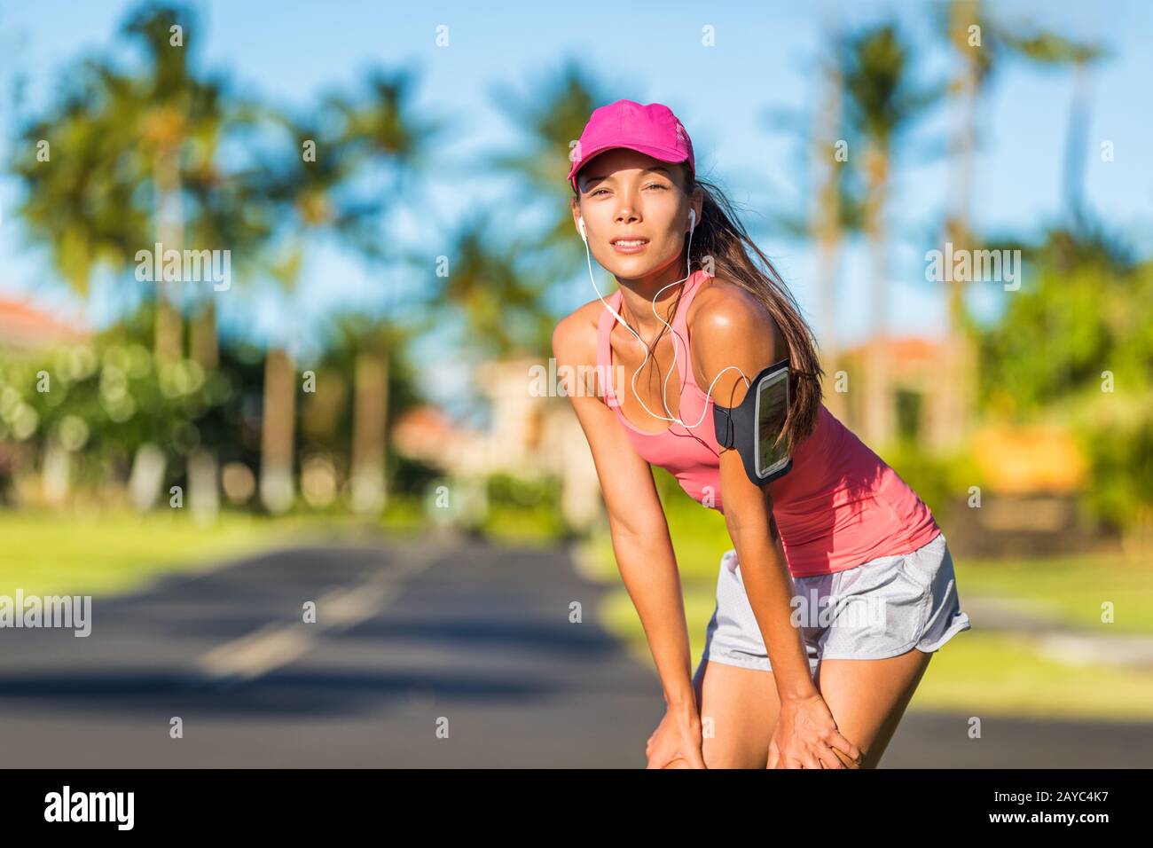 Femme coureur fatiguée prête à courir avec casquette de sport et brassard  de sport avec écouteurs pour écouter de la musique mobile. Une fille  asiatique active qui se repose sur une pause