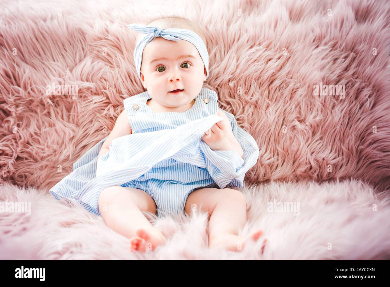 Cute smiling enfant sur un canapé rose. Premières dents de bébé 6 mois santé. Banque D'Images