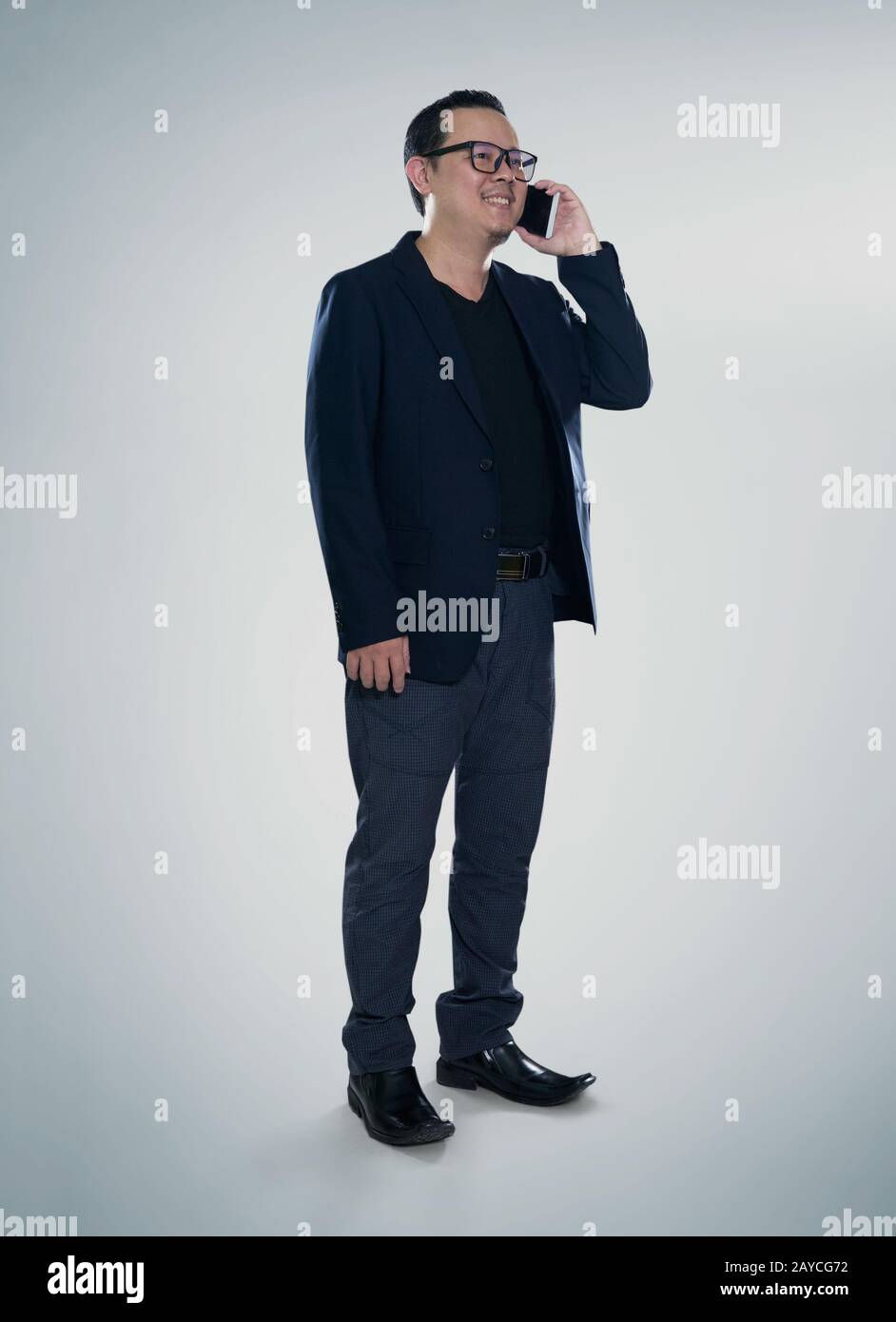 Un homme d'affaires souriant et heureux portant un costume noir et utilisant un smartphone moderne Banque D'Images