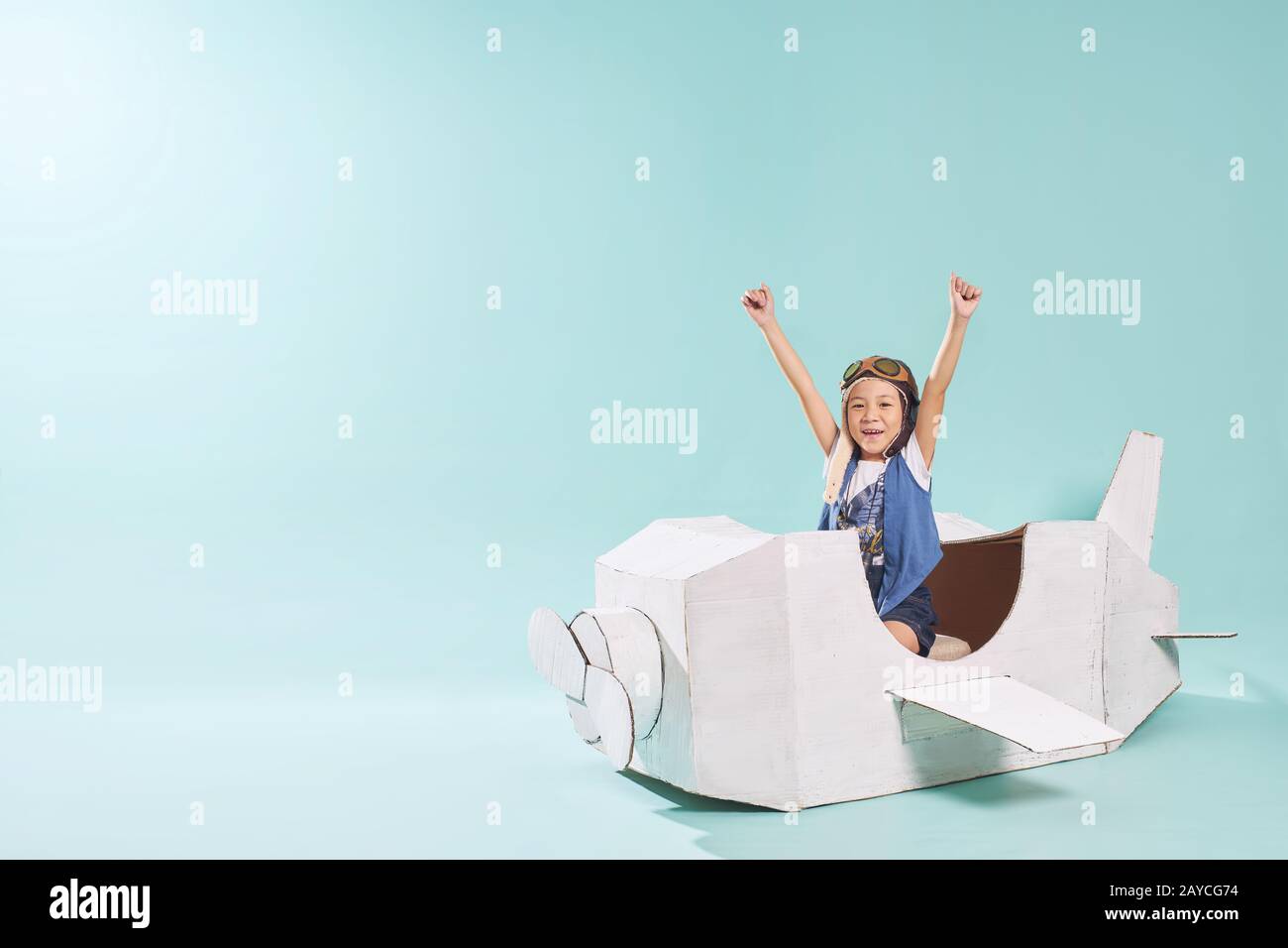 La petite fille asiatique est heureuse assise sur un avion en papier de carton fait à la main . Isolé sur fond vert menthe . Banque D'Images