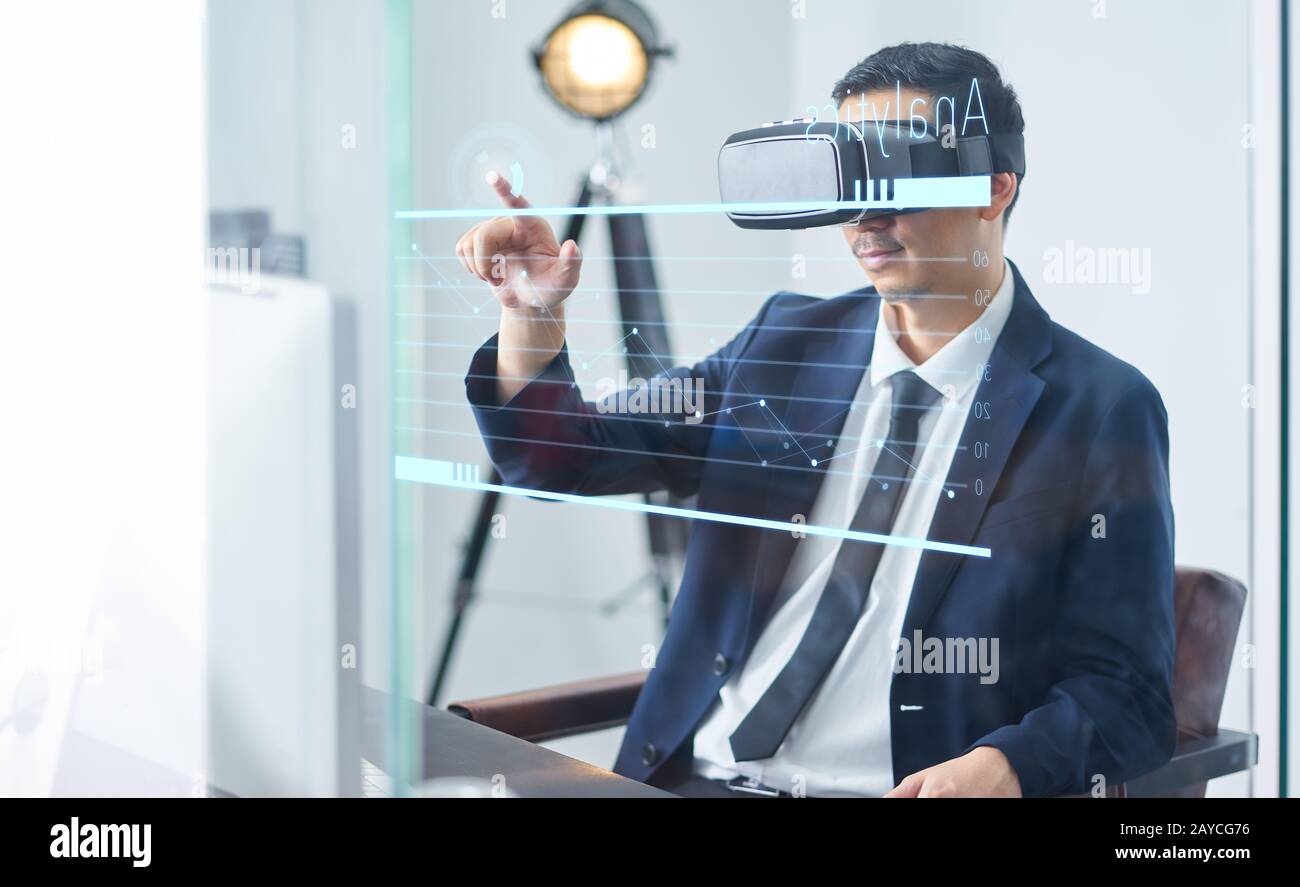 Homme d'affaires asiatique portant des lunettes de réalité virtuelle et pointant le graphique de croissance d'entreprise dans un bureau . Banque D'Images