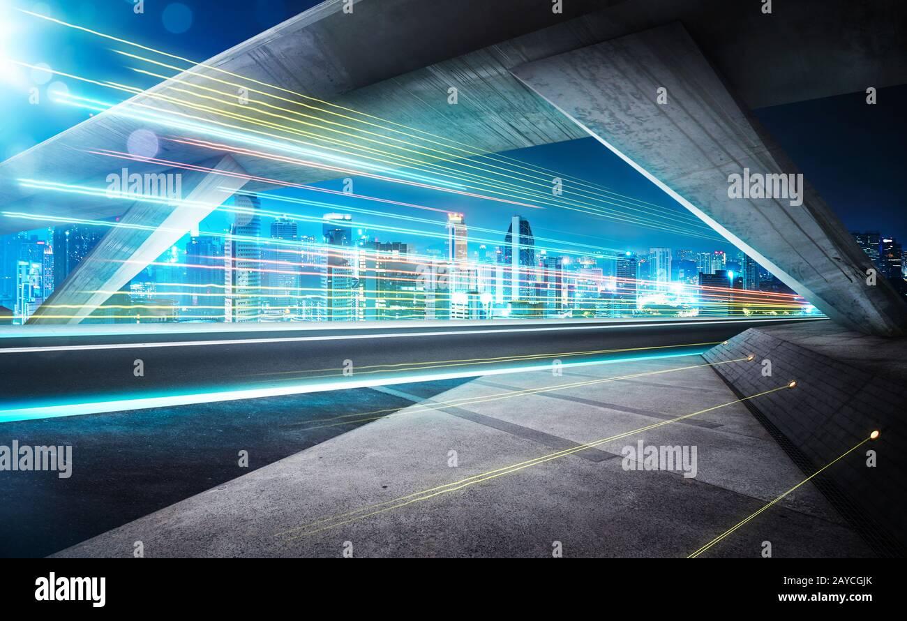 Vider la route asphaltée sous le pont pendant la nuit avec des sentiers légers et un magnifique horizon urbain arrière-plan . Banque D'Images
