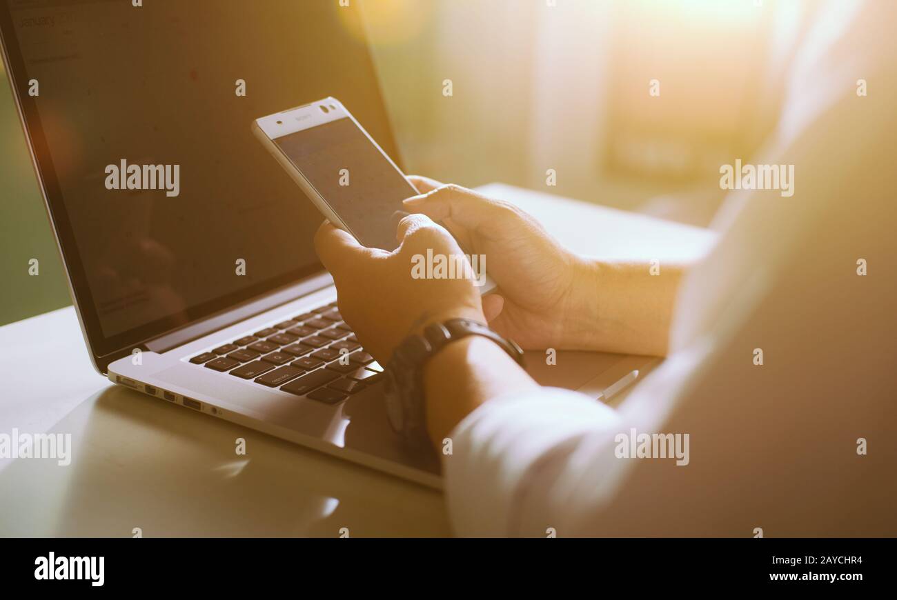 Silhouette d'une photo courte d'un jeune homme travaillant à domicile à l'aide d'un smartphone et d'un ordinateur portable Banque D'Images