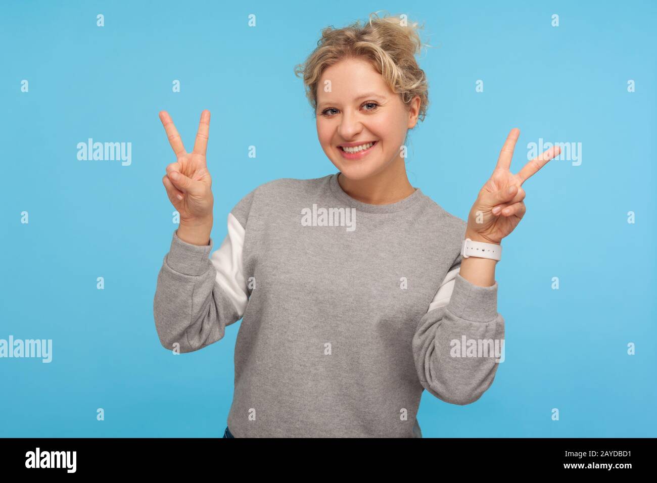 Une femme gaie excitée avec des cheveux courts en sweat-shirt montrant un geste de victoire, un double signe de paix, se réjouissant des résultats réussis, le but réalisé Banque D'Images