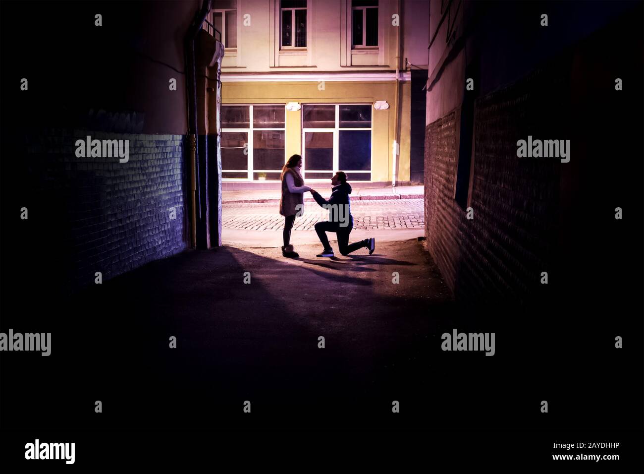 l'homme fait une proposition de mariage à une femme s'agenouillant dans la lumière à la fin d'une ruelle sombre Banque D'Images