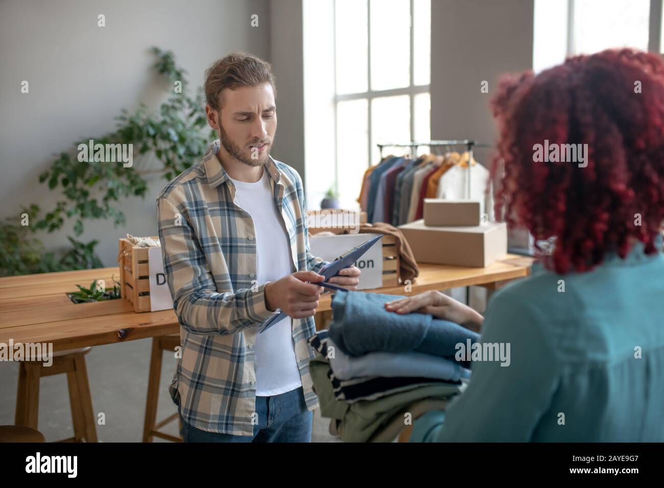 Jeune homme écrivant dans un carnet, près d'une femme avec des vêtements dans les mains. Banque D'Images