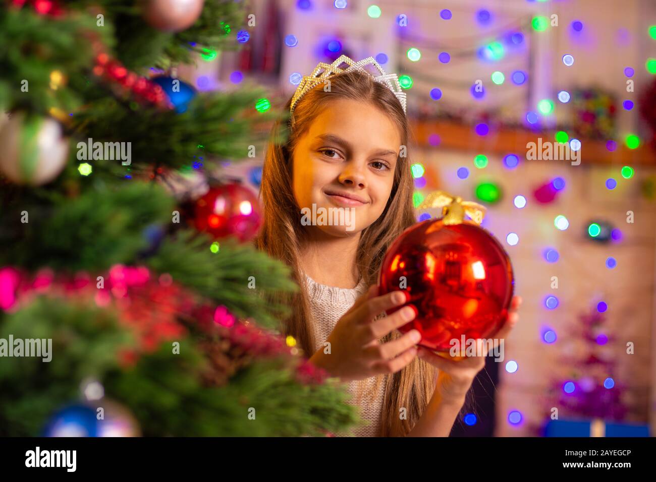 Belle jeune fille de 10 ans, avec une grosse boule rouge de derrière un  arbre de Noël Photo Stock - Alamy
