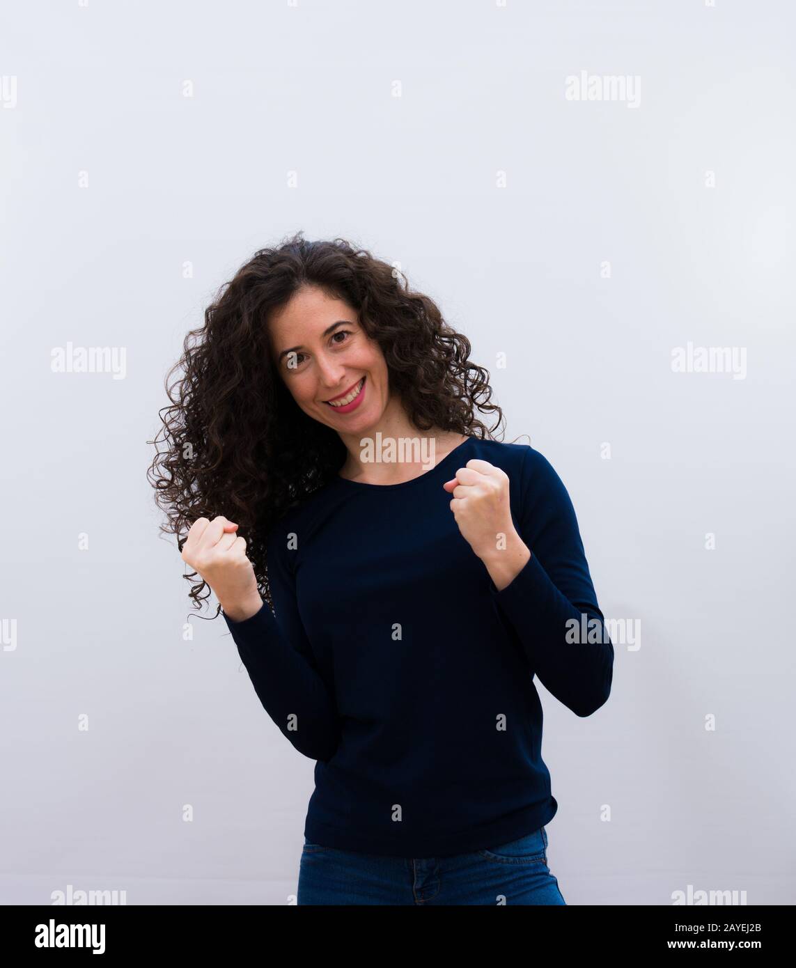 jeune jolie femme aux cheveux bouclés noirs criant triomphalement, regardant comme excitée, heureuse et surprise gagnant, célébrant contre le mur rose Banque D'Images