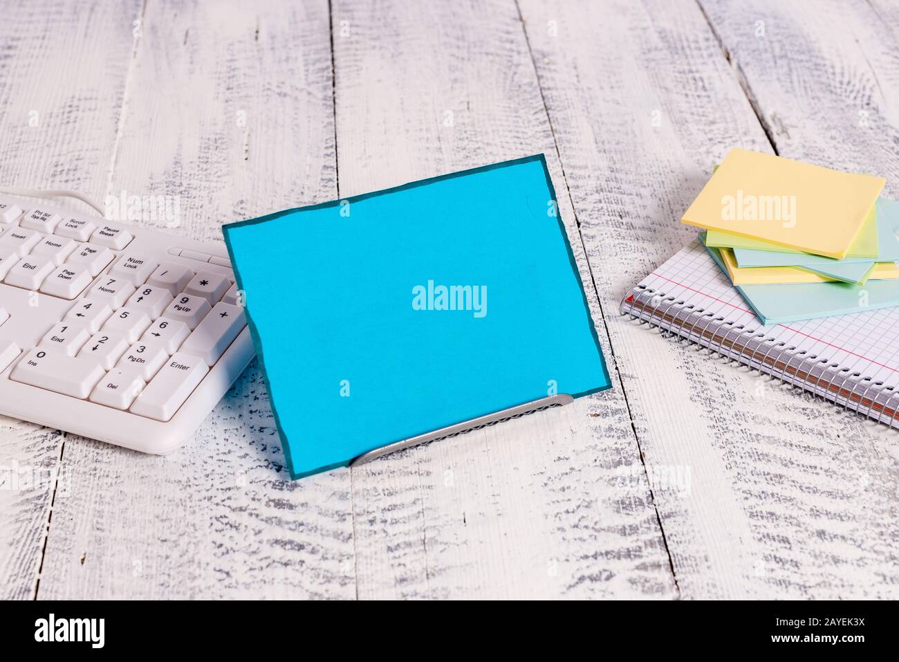 Notepaper en bleu se tenant sur un fil tampon entre un clavier et un livre de mathématiques. L'ancien papier de notation se trouve près de l'ordinateur Banque D'Images