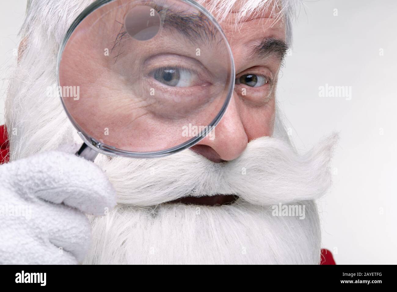 Le Père Noël regardant dans la caméra à travers une loupe Banque D'Images