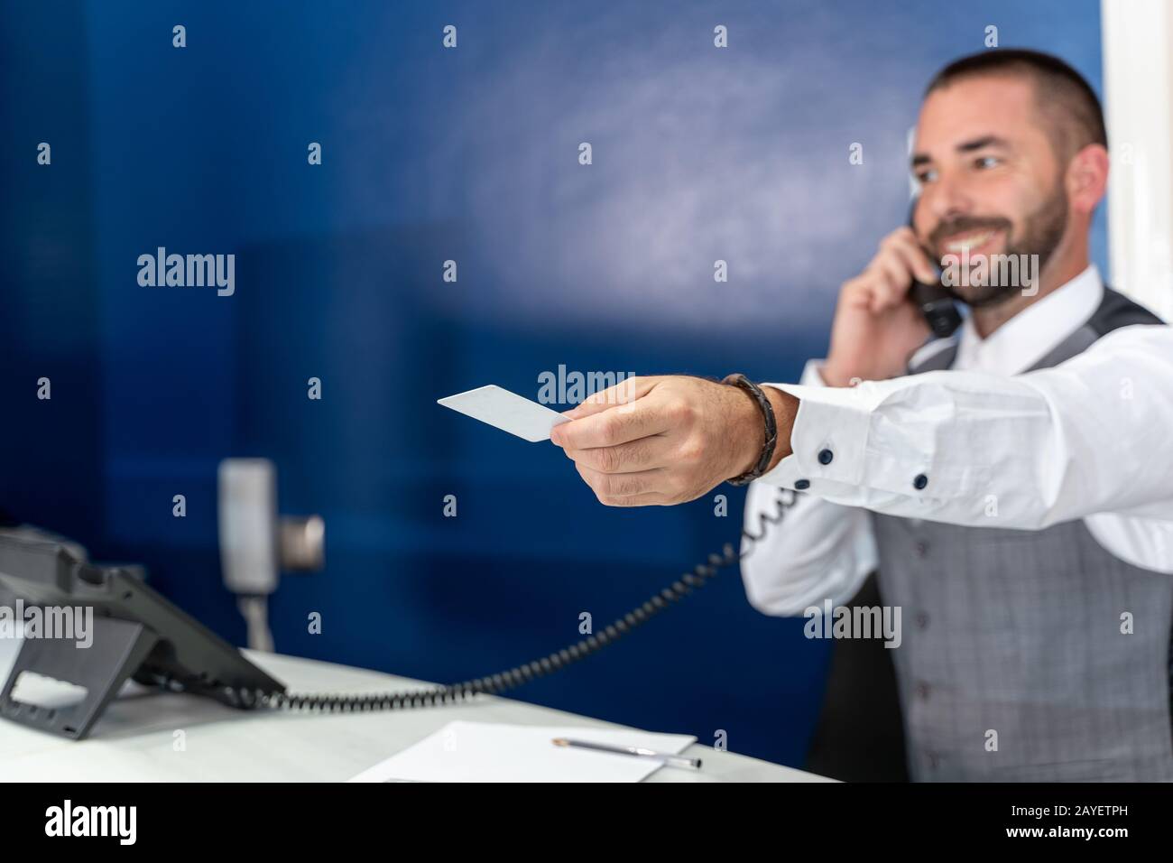 Faites le point sur la photo d'un réceptionniste qui parle au téléphone et souriait alors qu'il étend son bras avec une carte de chambre dans sa main Banque D'Images