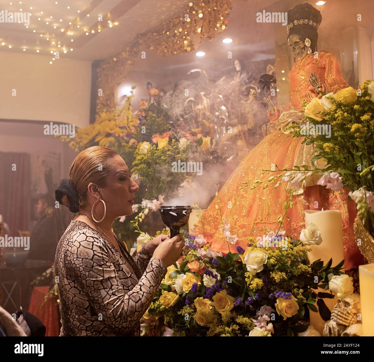 Une trans prêtresse souffle de la fumée aux statues de Santa Muerte dans un temple maison à Queens, New York City. Banque D'Images