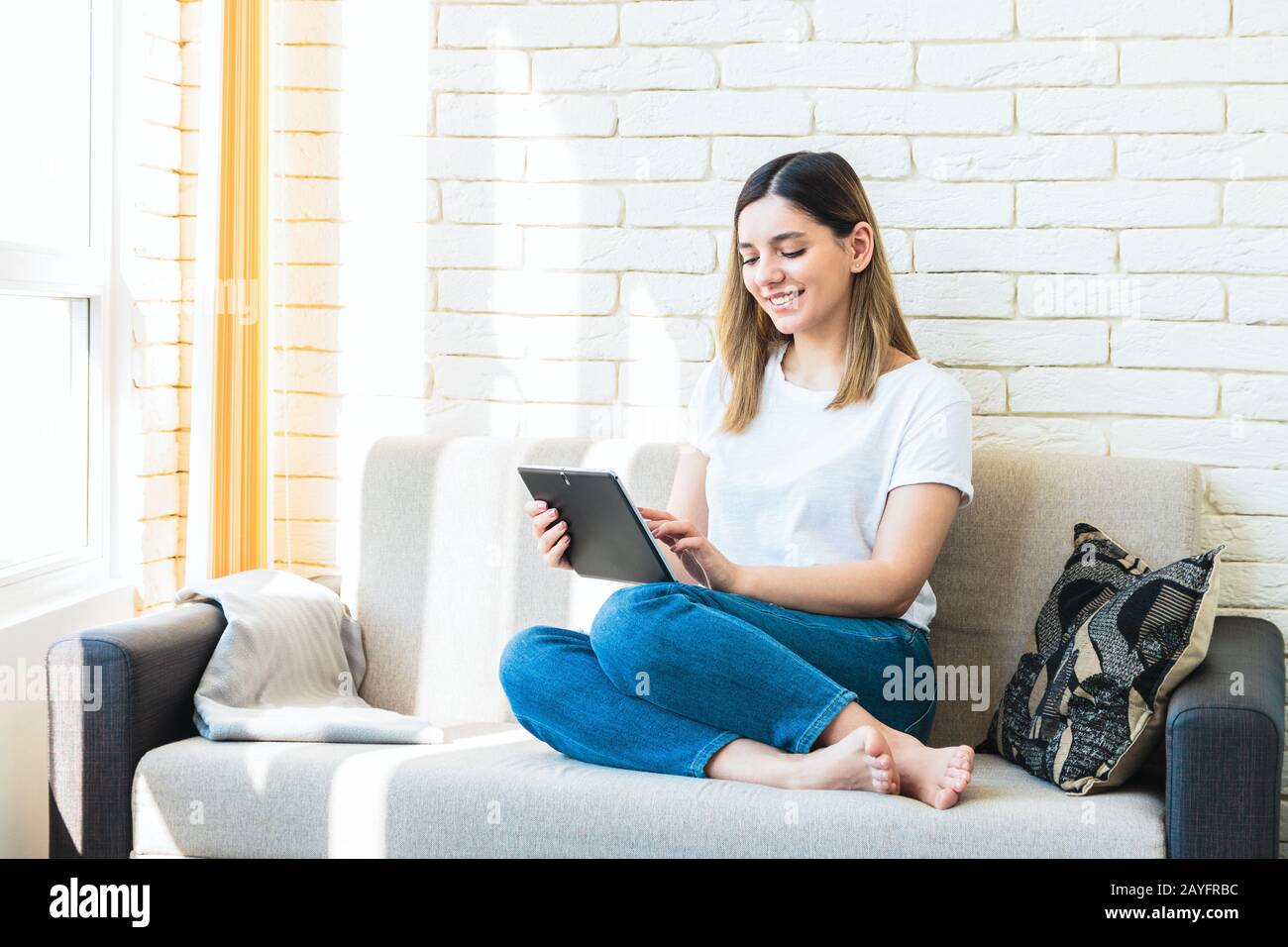 jeune femme gaie avec un beau sourire à la maison sur un canapé, en utilisant une tablette Banque D'Images