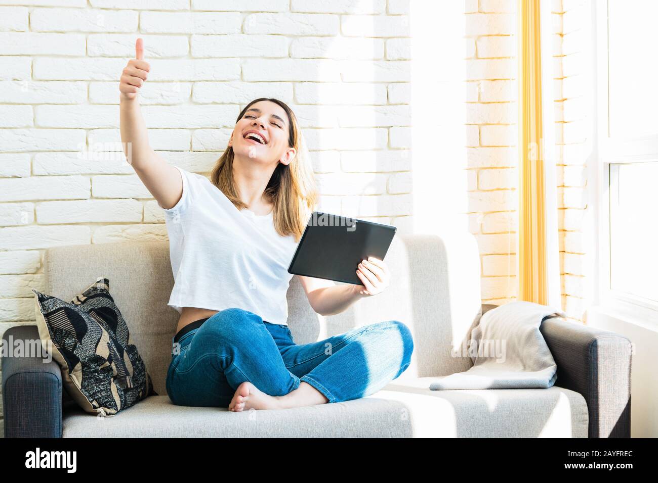 jeune femme gaie avec un beau sourire à la maison sur un canapé, en utilisant une tablette a gagné jouer en ligne Banque D'Images