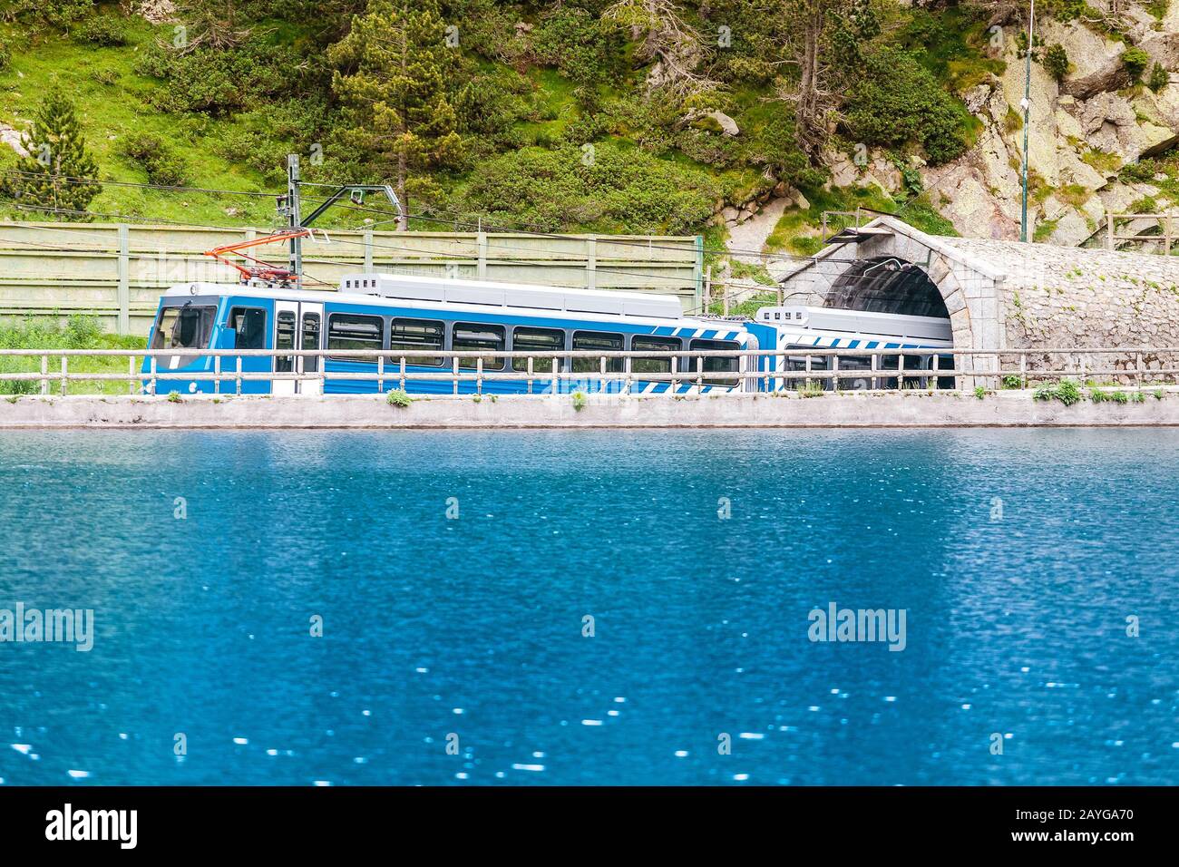 Train traversant la vallée de Nuria contre le premier plan du lac bleu de montagne, Espagne Pyrénées Banque D'Images