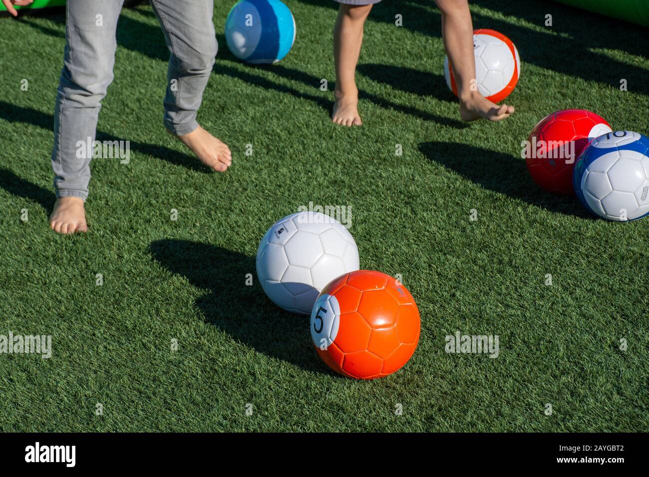 Des ballons de football et de football vibrants sur l'herbe verte avec des pieds pour enfants qui se piquent pour se divertir et s'amuser à l'extérieur. Banque D'Images
