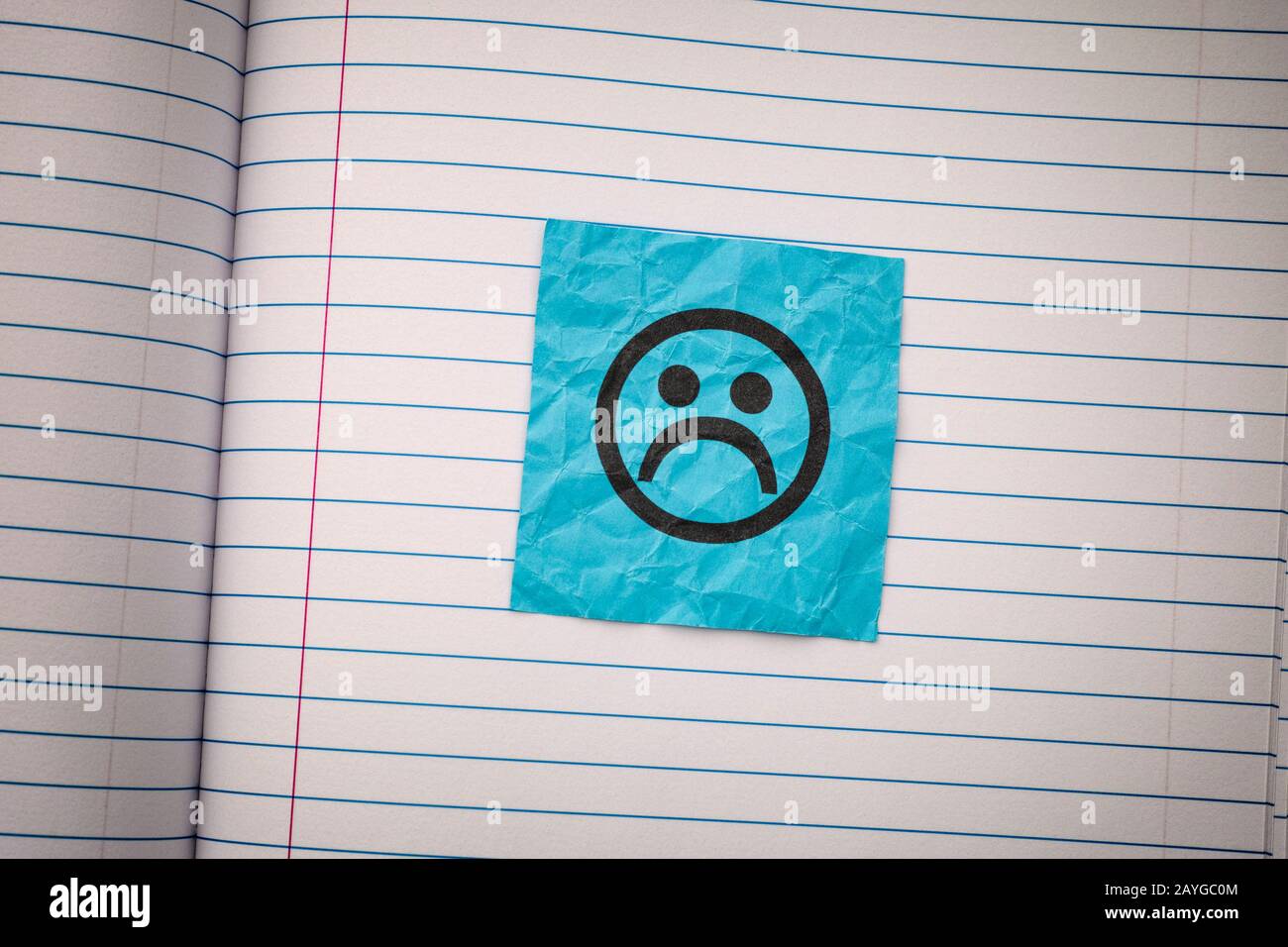 Note en papier bleu avec un visage triste sur un papier doublé. Gros plan. Banque D'Images