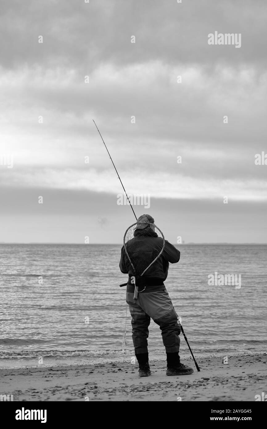 Pêcheur avec équipement complet debout sur une plage en regardant le coucher du soleil Banque D'Images