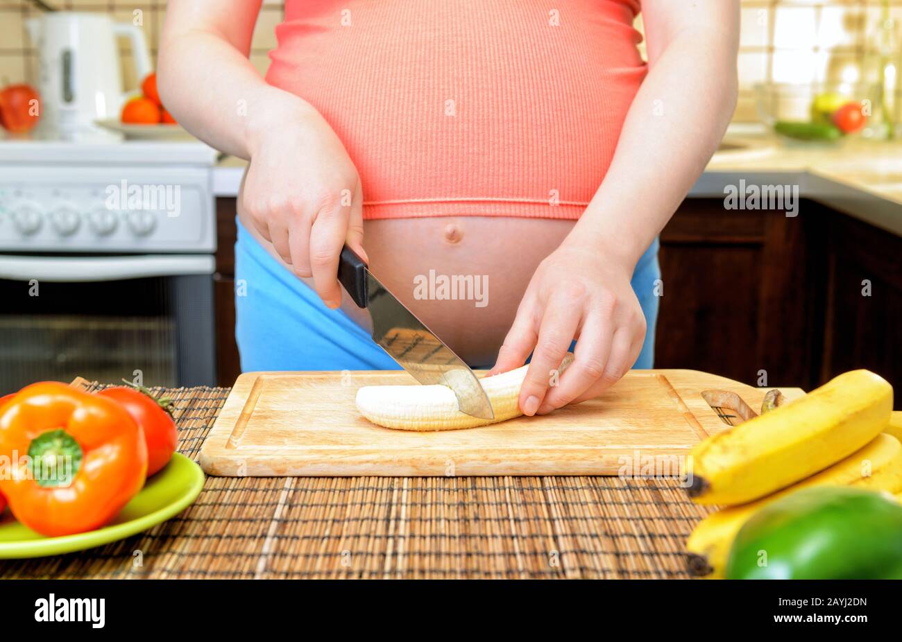 La femme enceinte prépare une banane dans la cuisine. Des aliments sains. Banque D'Images