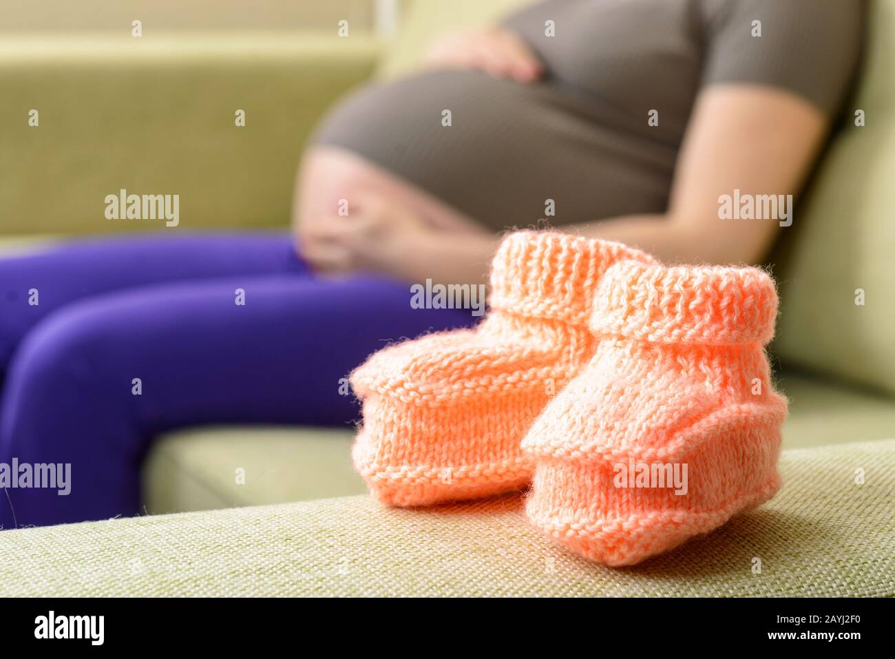 Une belle chaussures de bébé en laine sur le canapé à côté d'une femme enceinte Banque D'Images Une belle chaussures de bébé en laine sur le canapé à côté d'une femme enceinte Banque D'Images