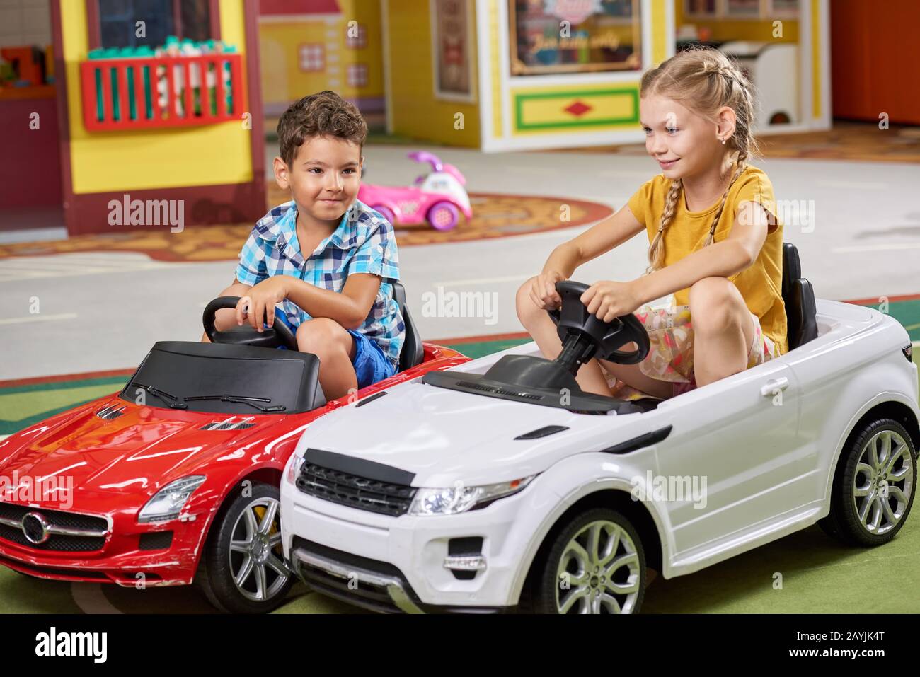 Enfants jouant ensemble assis dans des voitures de jouet. Banque D'Images