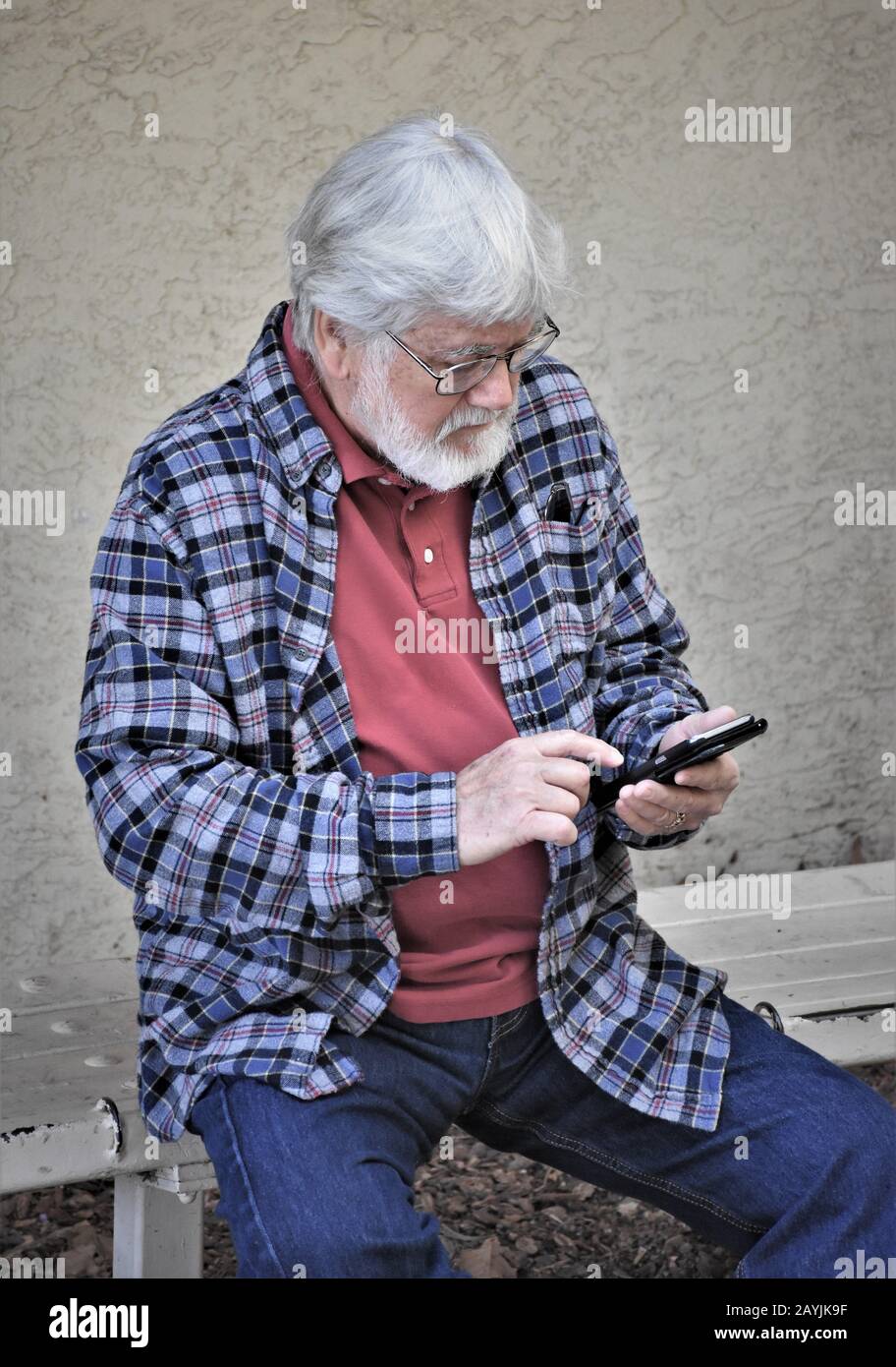 Homme senior assis et essayant de comprendre son vrai nouveau téléphone cellulaire et tous ses changements et avancées avec la barbe et les lunettes en Californie États-Unis Banque D'Images