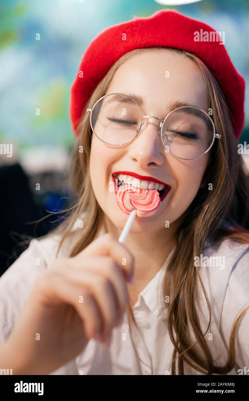 Jeune fille mangeant un bâton collant sucré en France café en béret rouge  et verres. Les caries conceptuelles et les dommages sont un danger pour  l'émail des dents Photo Stock - Alamy