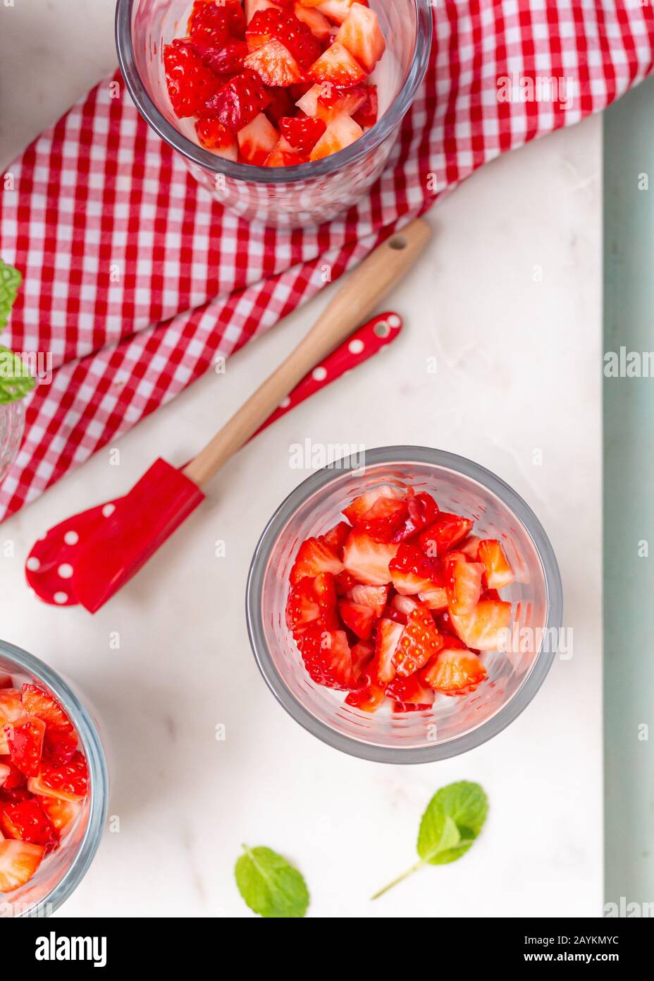 Vue en hauteur d'un verre sain et antioxydant plein de morceaux de fraise avec miel et chia. Une serviette colorée et une cuillère illuminent la scène. Banque D'Images