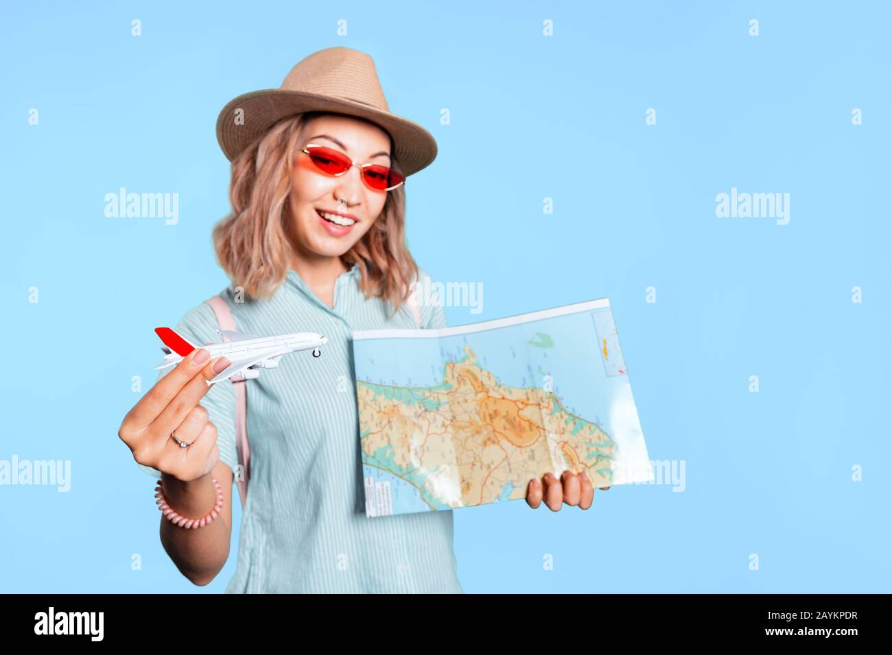 Heureuse femme asiatique avec carte et avion jouet en studio contre fond de couleur Banque D'Images