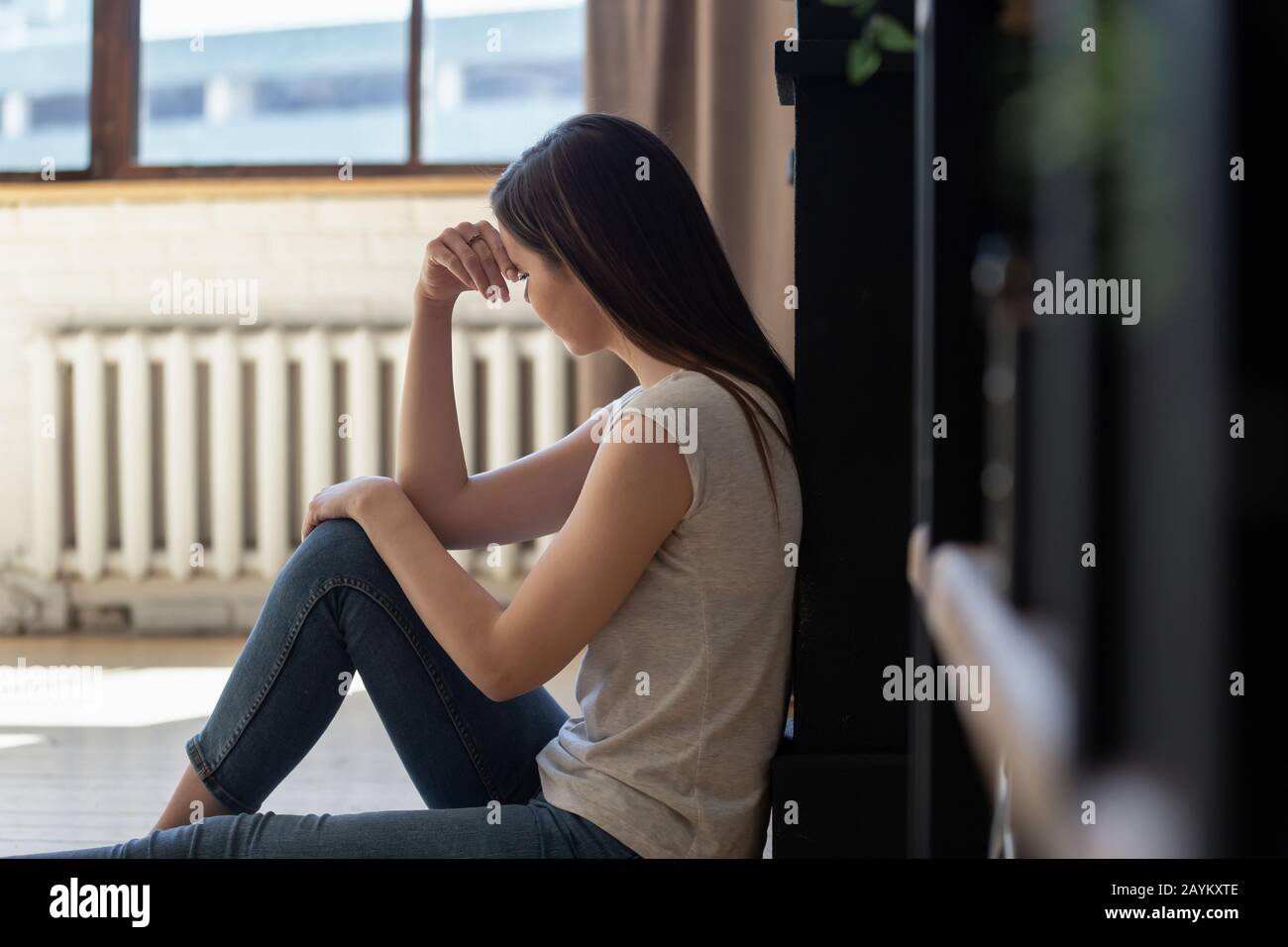 Une jeune femme triste est assise sur le sol perdue dans les pensées souffrant Banque D'Images
