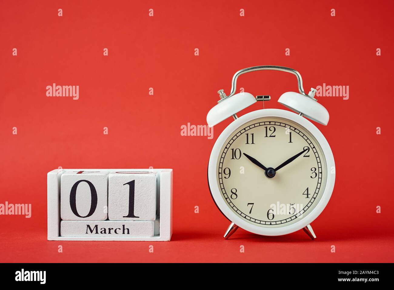 Réveil rétro blanc avec cloches et blocs calendrier en bois avec date du 1er mars sur fond rouge Banque D'Images