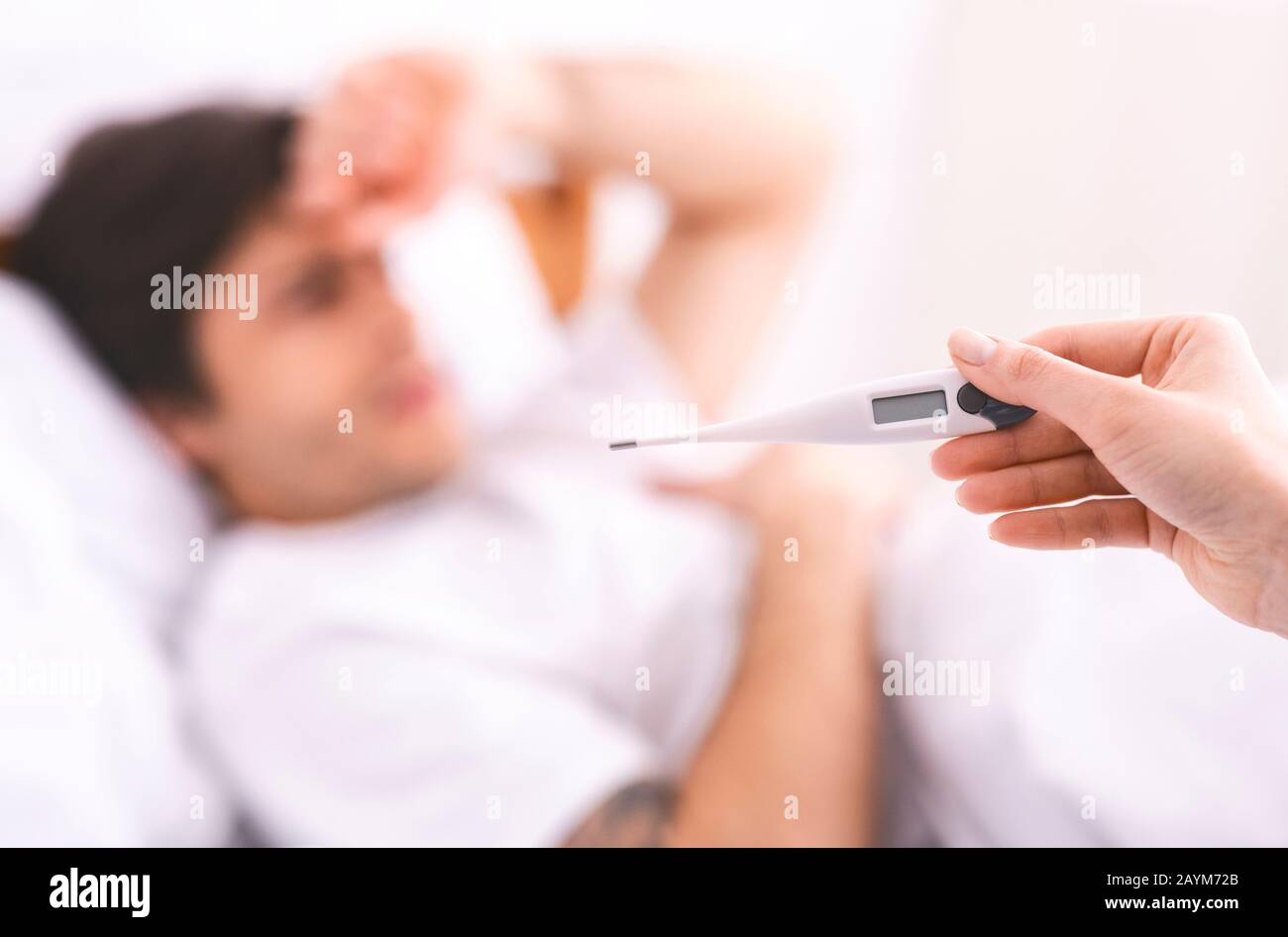 Mari malade allongé dans le lit, femme bienveillante vérifiant sa température Banque D'Images