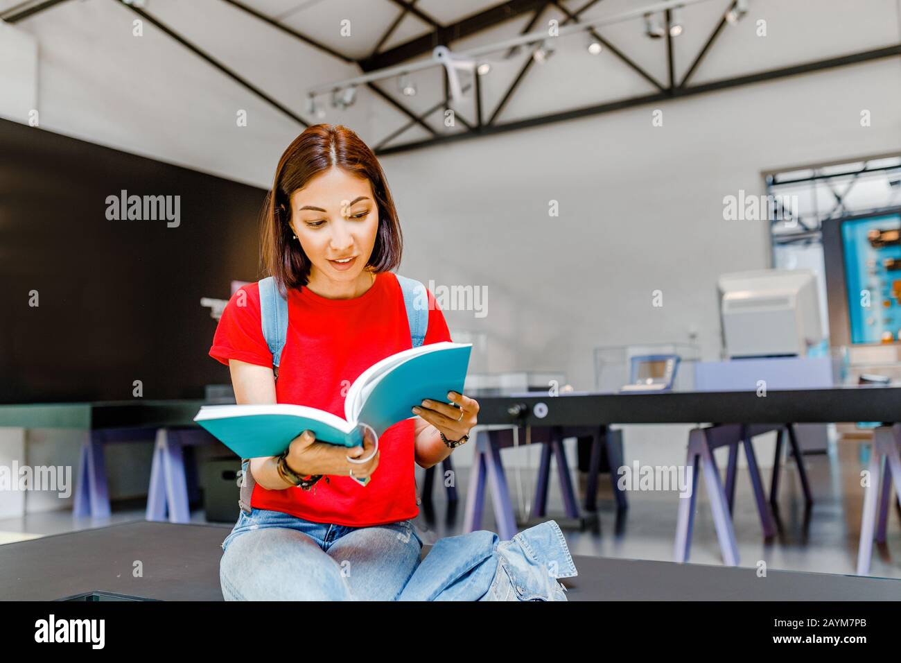 une jeune étudiante en lecture d'un livre dans une bibliothèque moderne à l'intérieur de l'université Banque D'Images