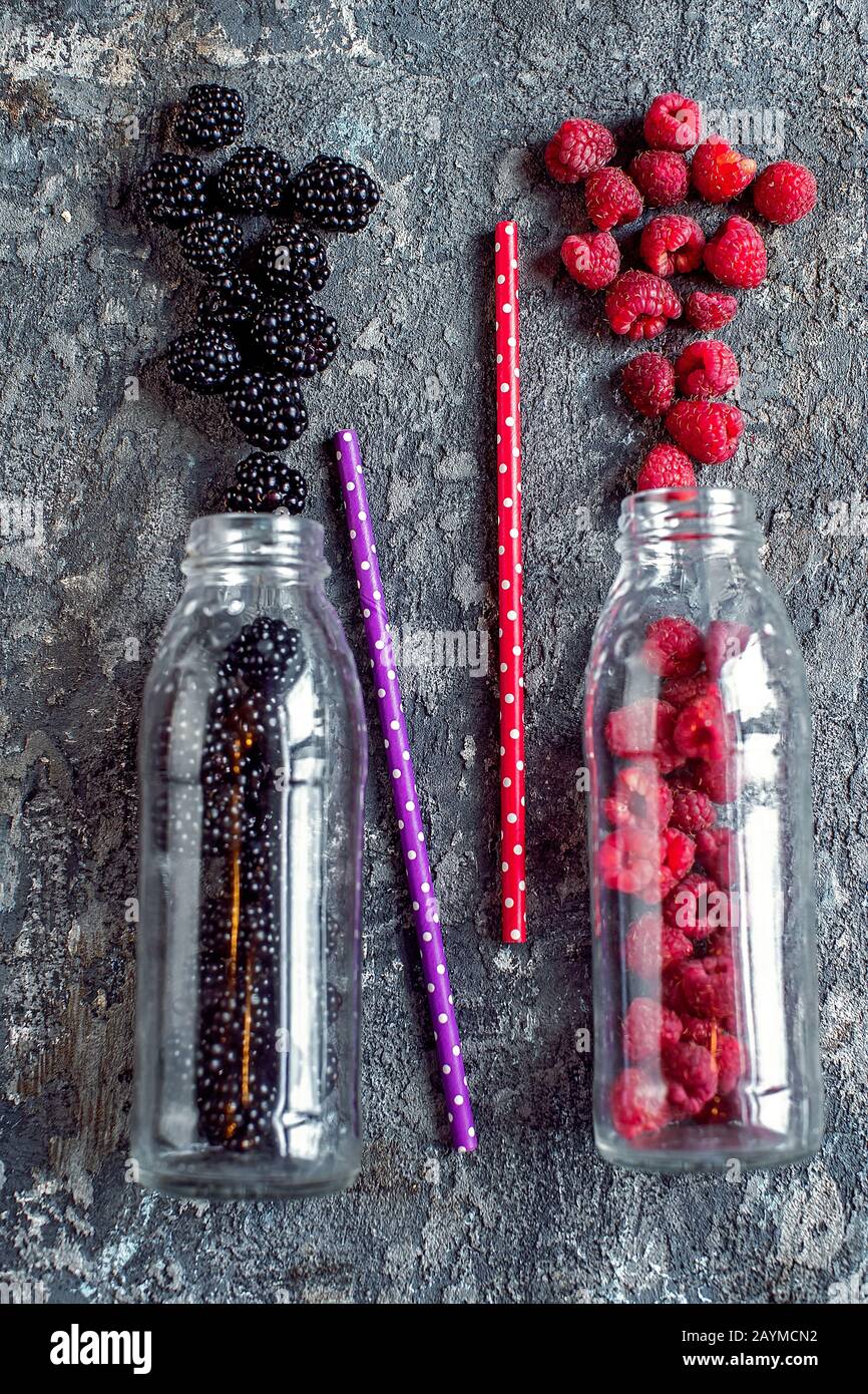 Fruits mûrs et framboises en bouteilles de verre avec pailles sur fond de pierre. Ingrédients à base de smoothie bio frais. Concept de nourriture alimentaire pour la santé ou le détox. Banque D'Images