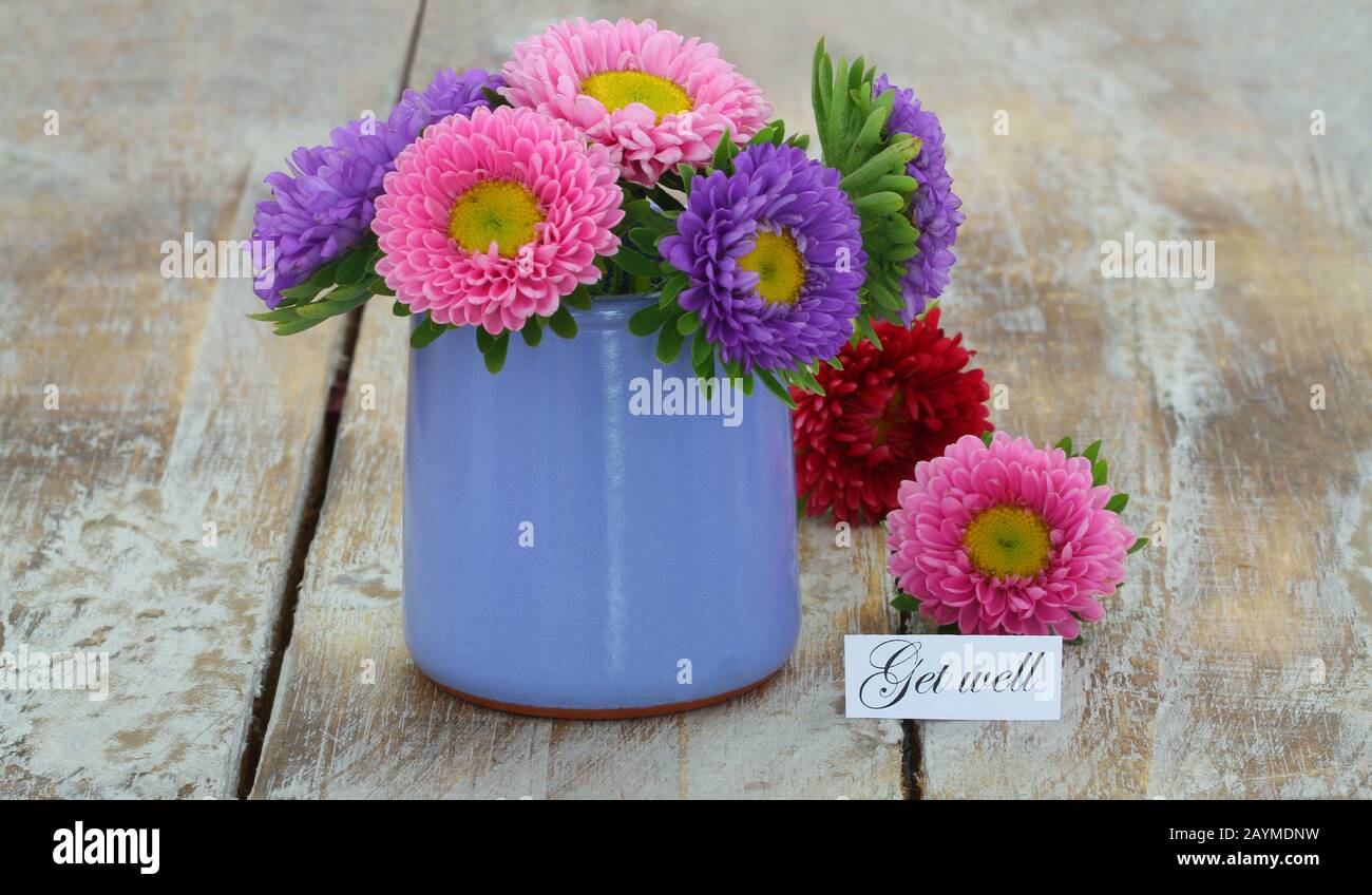 Obtenez une carte de puits avec des daisies colorées dans un vase bleu sur une surface rustique en bois Banque D'Images