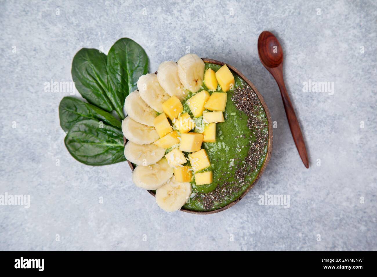 bol aux épinards smoothie avec banane et mangue, graines de chia dans des bols à la noix de coco sur un fond en béton gris. vue de dessus. Banque D'Images