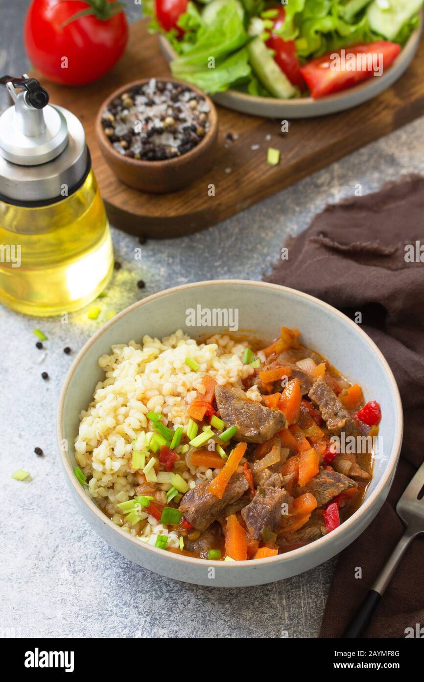 Concept de saine alimentation. Compote de bœuf avec légumes en sauce bulgur et salade de légumes frais sur un plateau de table en pierre légère. Banque D'Images