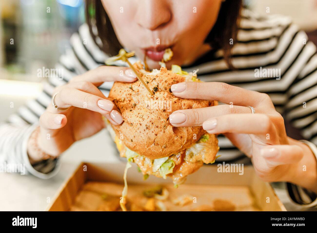 Femme mangeant un hamburger dans un café moderne fastfood, concept de déjeuner Banque D'Images