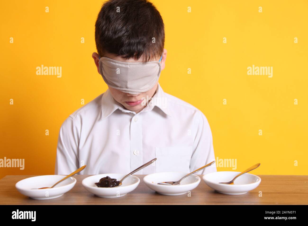 Test de goût à l'aveugle, jeune garçon de 12 assis avec des plats d'échantillon de nourriture pour goûter différentes denrées alimentaires bandés Banque D'Images