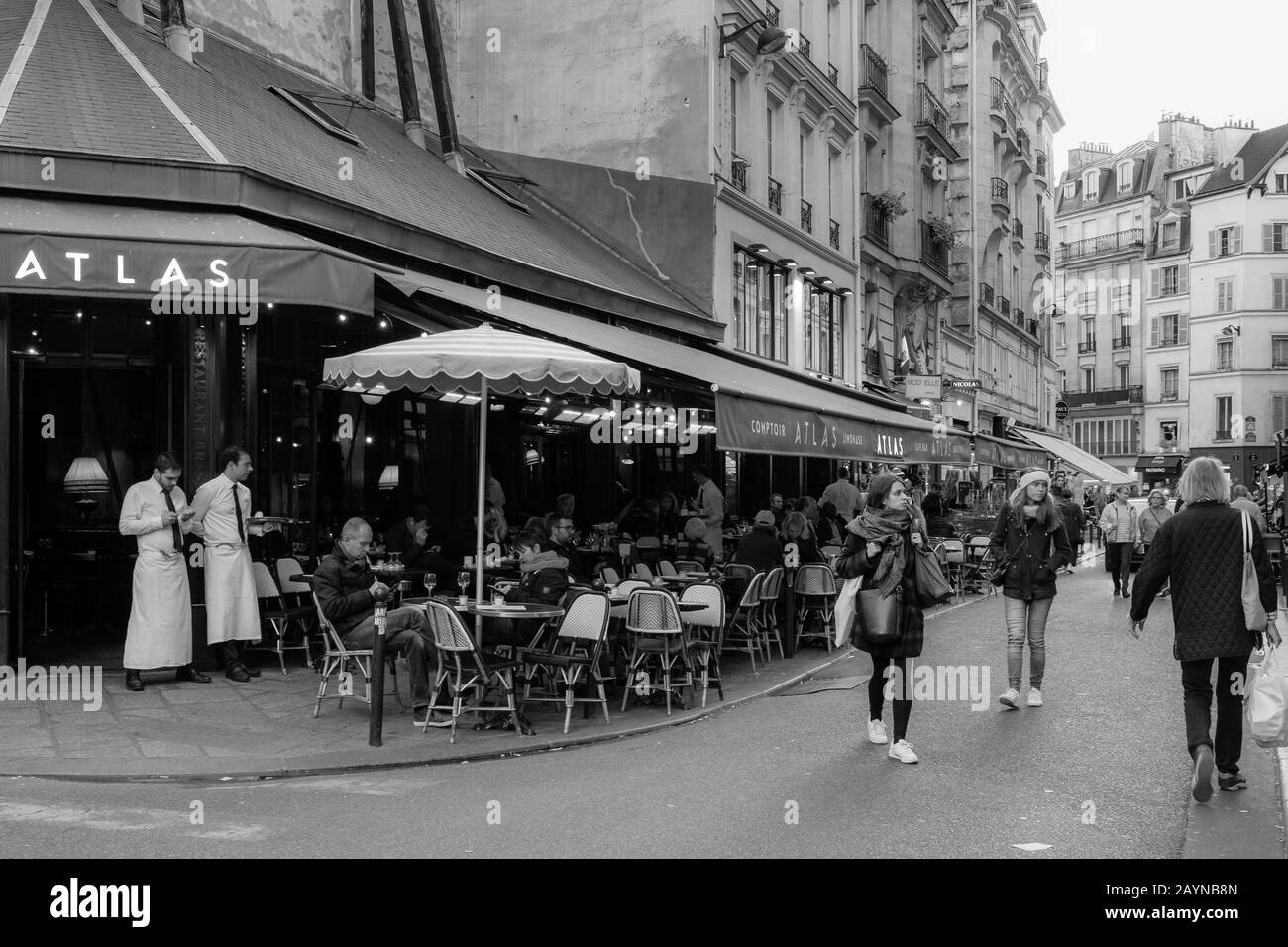 Une scène de rue noire et blanche à Paris avec des habitants assis à l'extérieur dans un restaurant et des gens qui marchent dans la rue Banque D'Images