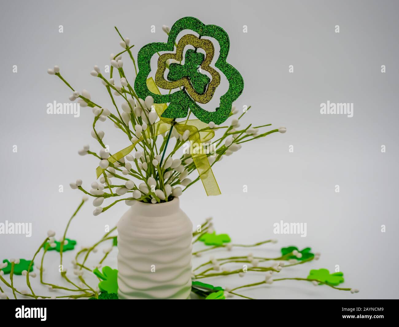 Décoration de la Saint-Patrick, vase blanc rempli de fleurs blanches ornées de perles et grand trèfle à quatre feuilles vert étincelant entouré de plus petits clov à quatre feuilles Banque D'Images