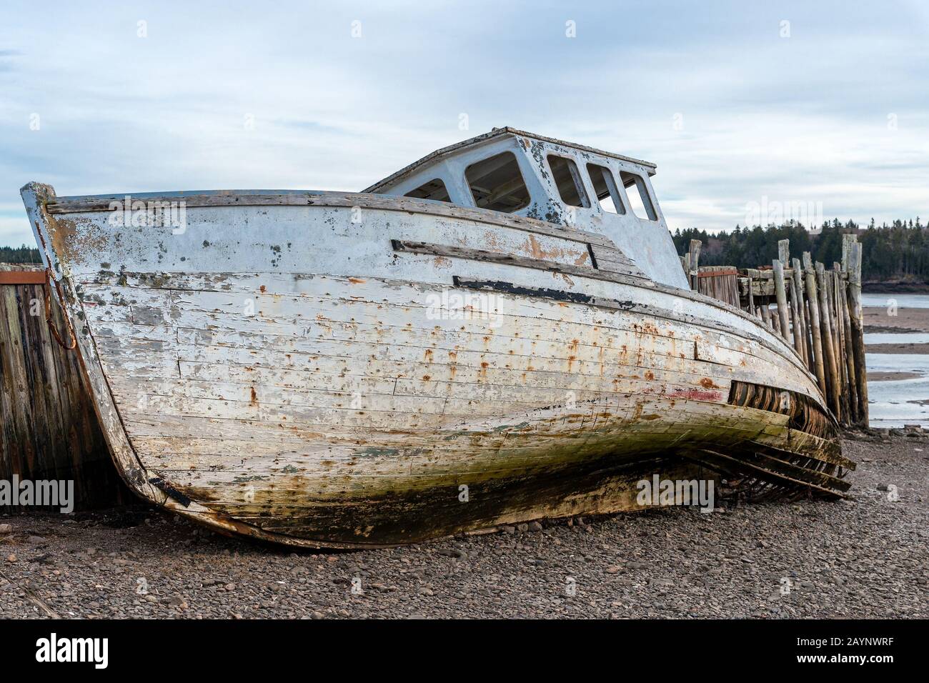 Un bateau naufragé sur la rive à côté d'un quai délabré. Le bateau et le quai sont en très mauvais état et se déforment. Vue gros plan. Marée basse. Banque D'Images