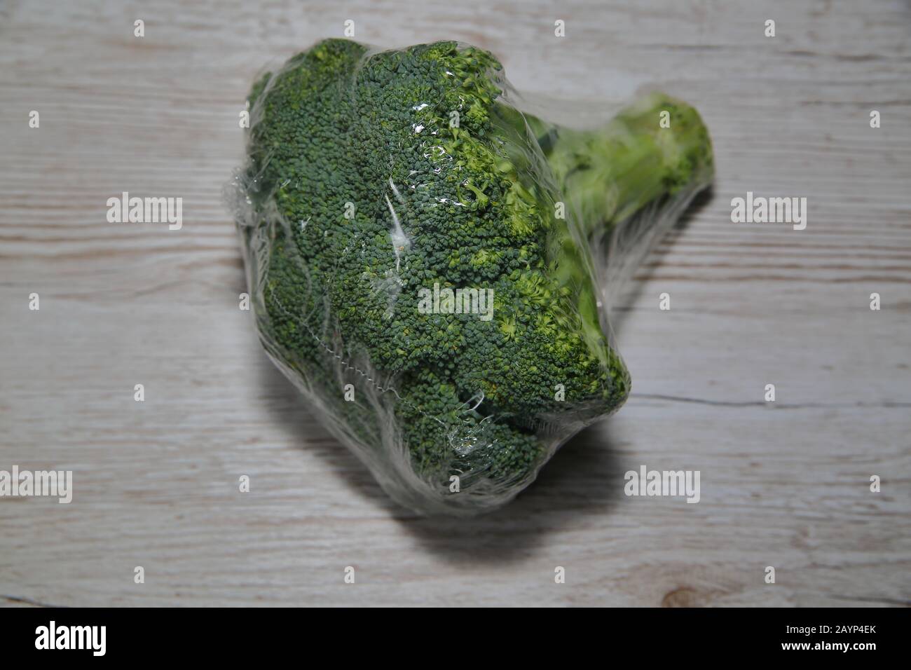 Le brocoli frais vendu au supermarché sous forme de bio, écoemballé en feuille de plastique, se trouve isolé sur la table en bois de gros plan Banque D'Images