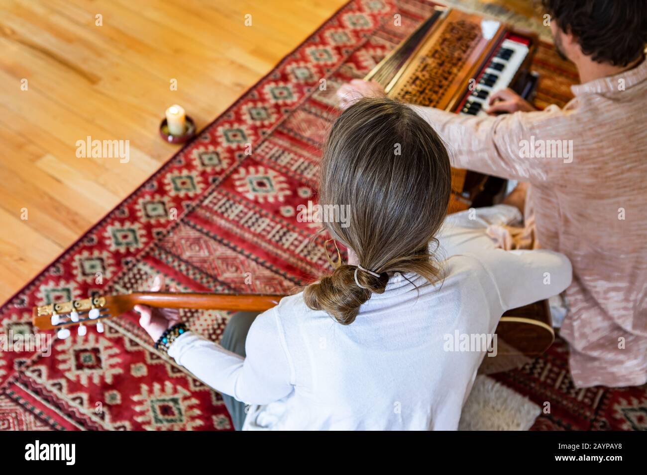 Jeune homme et femme jouant de la musique apaisante à l'aide de la guitare classique et de l'harmonie avec la bougie brûlant et assis sur le tapis de sol dans la chambre Banque D'Images